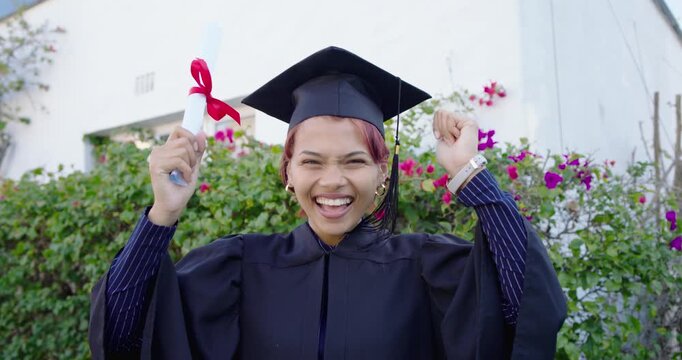 African American woman celebrating graduation on campus in gown and cap, waving red ribbon scroll