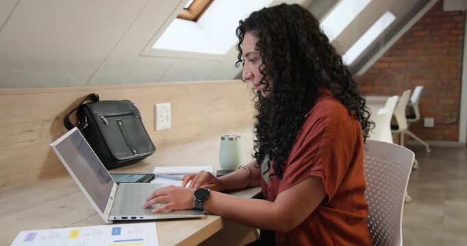 African American woman referencing laptop writing typing and comparing documents on screen at loft