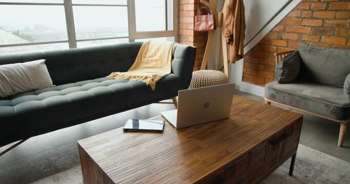 Camera is starting to pan right, revealing wooden coffee table with open laptop for workspace shot