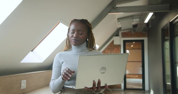 Mid-adult woman wearing gray sweater typing on silver laptop in loft, pausing to check corridor