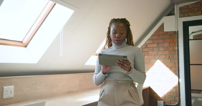 African woman in turtleneck and trousers holding tablet, checking skylight, rehearsing talk in loft