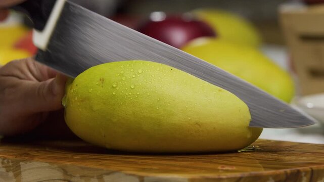 Person slicing off chunk of juicy mango and cutting up squares, closeup shot in slow motion