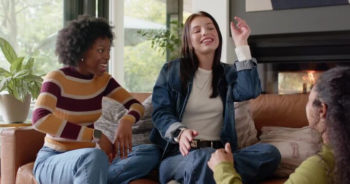 Diverse female friends mimicking left woman's gestures, laughing during lighthearted chat on sofa