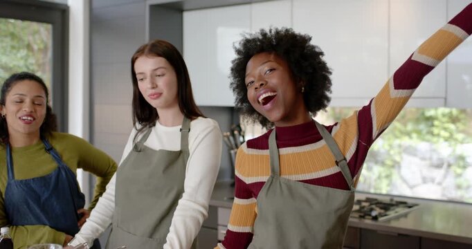 Diverse female friends camera rolling, filming recipe at kitchen island with mixing bowls, aprons