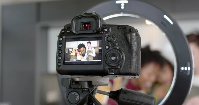 Diverse female hosts wearing aprons filming recipe steps at counter while DSLR pulling back