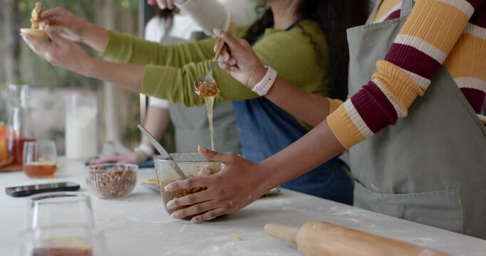 Diverse female friends making recipe at counter, stirring in bowl, right woman testing, copy space