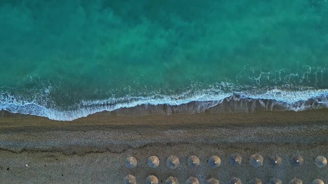 Aerial view of a sandy beach with rows of parasols along the turquoise shoreline in Greece.