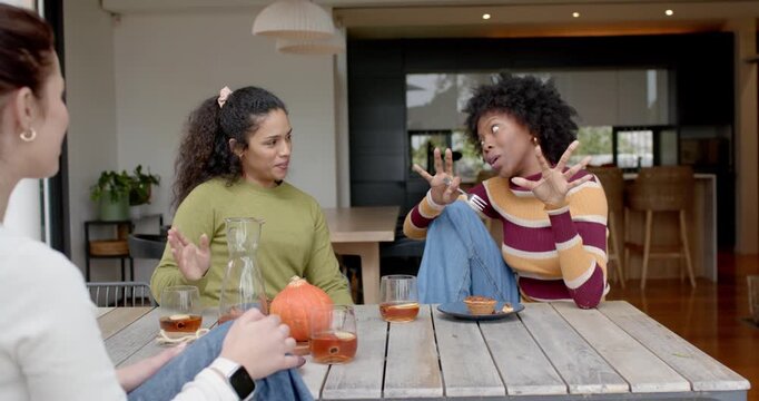 Female friends watching right woman in striped top starting story, gesturing fork to amuse at patio
