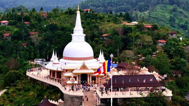 Aerial view of a white Buddhist stupa surrounded by lush green hills and trees in Sri Lanka.
