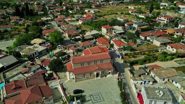 Aerial view of a traditional village with a central stone church featuring red-tiled roofs and a small town square surrounded by houses in Greece.