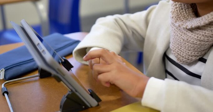 African American teen female placing hands tapping tablet at class desk doing work pausing resting