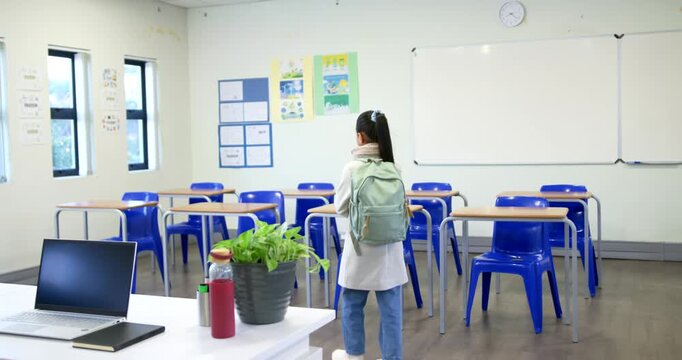 African American teen entering classroom adjusting backpack retrieving tablet sitting to study