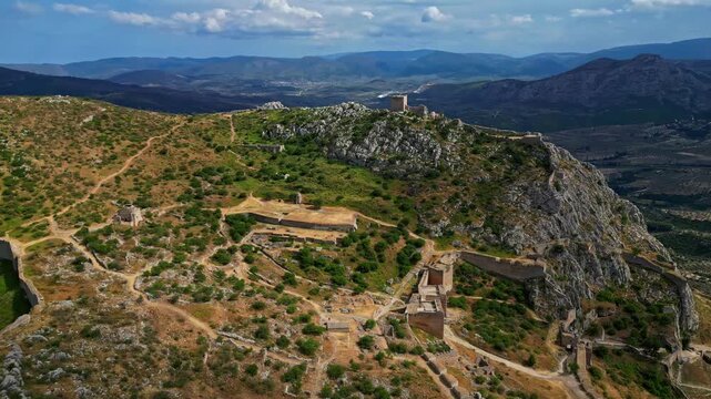 Aerial view of the historic Acrocorinth fortress ruins situated on a rocky mountain peak with ancient stone walls and fortifications overlooking the landscape in Greece.
