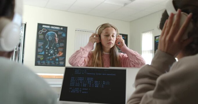 Diverse teens in class starting, female teen putting white headphones adjusting reading laptop code