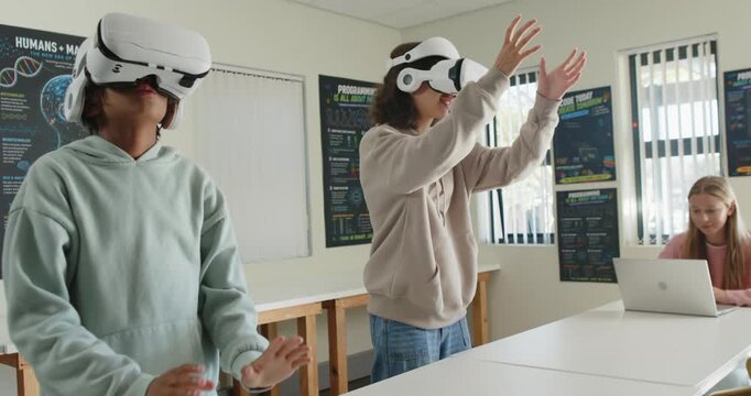 Teenage females at school donning VR headsets, reaching, exploring VR world while peer using laptop