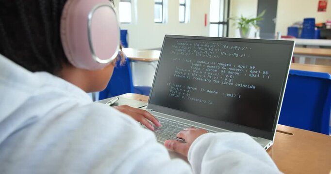 Teen student seeing code changes on laptop in class, typing and tuning pink headphones, copy space