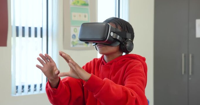 Wearing VR headset, red hoodie, African American teen gesturing and manipulating VR UI in classroom