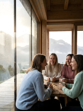 Grupo de amigas sonrientes disfrutando de una bebida caliente en una acogedora caba&ntilde;a de madera con vistas a la monta&ntilde;a en un d&iacute;a de lluvia