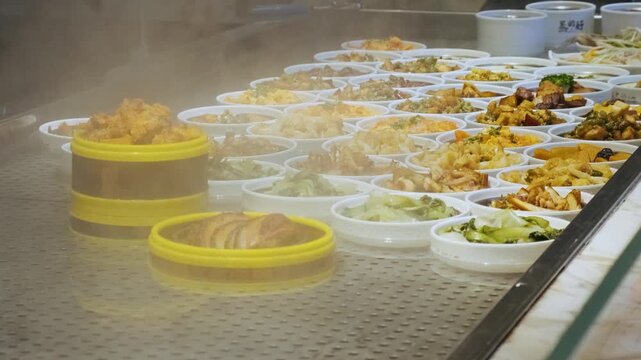 Steam rising above freshly prepared Chinese buffet meals. Food dishes displayed in bowls at buffet counter with variety of freshly prepared local cuisine. Traditional Asian meals ready for customers