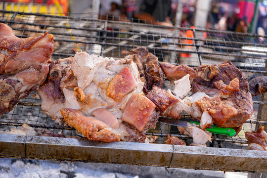 Pork cuts browning on a charcoal grill at a street food fair, traditional Peruvian cooking
