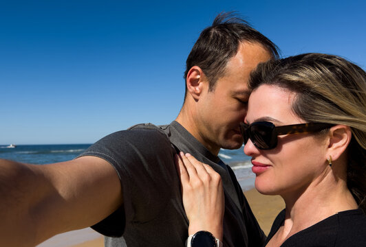 Cheerful young interracial couple embracing on the beach, laughing and enjoying a romantic summer vacation by the ocean. Concept of love, freedom, and happy relationships.