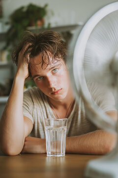 Exhausted person resting with their head on a table during a hot summer day, with a small fan blowing cool air nearby