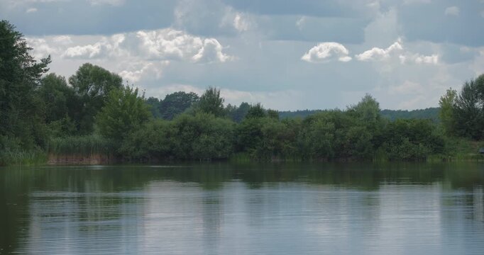 Static tripod shot of a scenic lake with forest reflection under cloudy sky