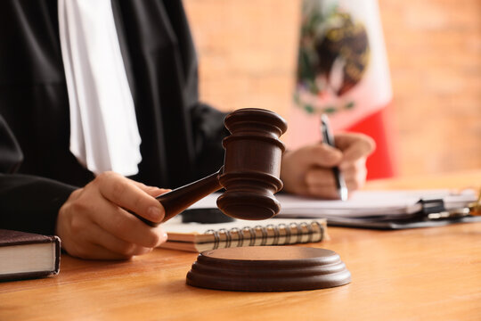 Judge holding a wooden gavel in a courtroom with a Mexican flag in the background, justice and law