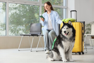Siberian husky dog sitting patiently with a woman and yellow suitcase in a waiting area, pet travel and companionship © Pixel-Shot