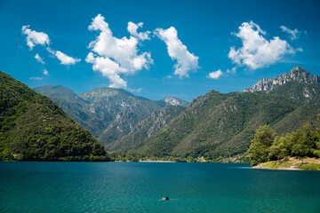 Obraz premium Swimmer in clear Lago di Ledro (Ledrosee) near Mezzolago and Molina di Ledro with mountain peaks and village shore ideal for summer travel