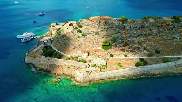 Aerial view of the historic Spinalonga fortress surrounded by turquoise waters and rocky terrain in Crete, Greece.