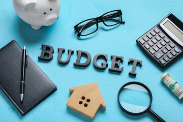 Budget word with financial planning tools, calculator, piggy bank, and house model on a blue...