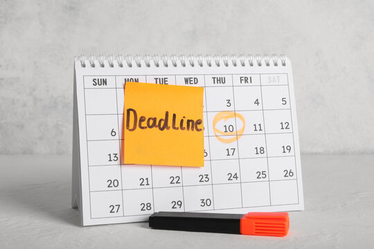 Paper calendar with marked date and word DEADLINE on white grunge table