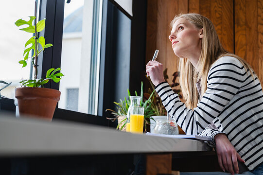 Relaxed woman enjoying a quiet morning with breakfast and a notebook by the window. Mindfulness, healthy habits, self-care, creativity and everyday home living concept