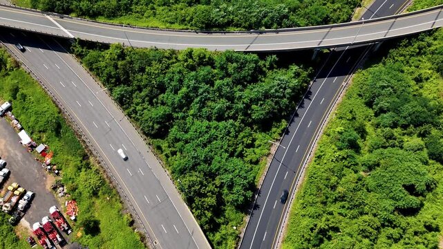Aerial view of highway overpass with cars moving through dense green forest, representing transportation infrastructure, mobility, travel, and connectivity.