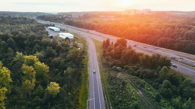Aerial view of highway traffic moving through forest at sunset, representing transportation, travel, infrastructure, mobility, and connectivity.