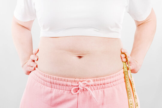 Overweight person measuring waist with tape on white background, representing body measurement, weight management, fitness, diet, health and wellness concepts.