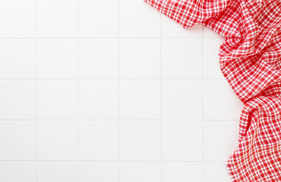Red checkered kitchen cloth on white tile background with copy space, suitable for food, cooking, recipe, restaurant, cafe and culinary design concepts.