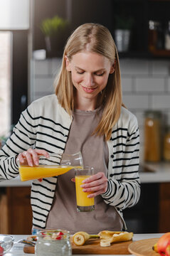 Young woman pouring fresh orange juice during a healthy breakfast in a modern kitchen. Balanced nutrition, wellness, morning routine and healthy lifestyle concept