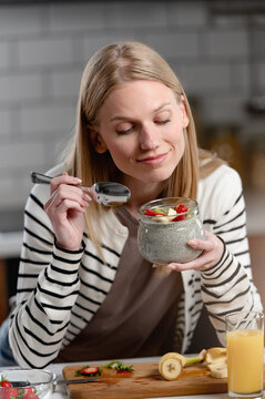 Young woman enjoying homemade chia pudding with fresh strawberries and banana in a cozy kitchen, promoting healthy eating, wellness and mindful breakfast habits