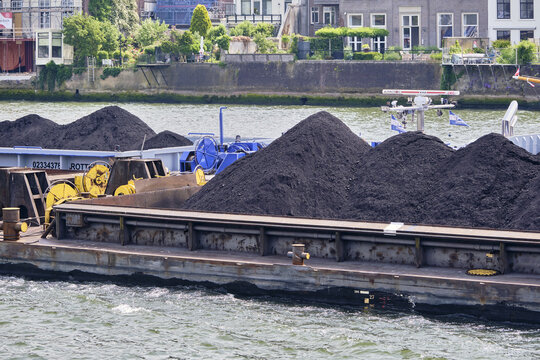 Dordrecht, Netherlands - 31 May 2026: View of a barge loaded with piles of coal navigating the Oude Maas river, highlighting industrial trade and bulk transport in the Netherlands.
