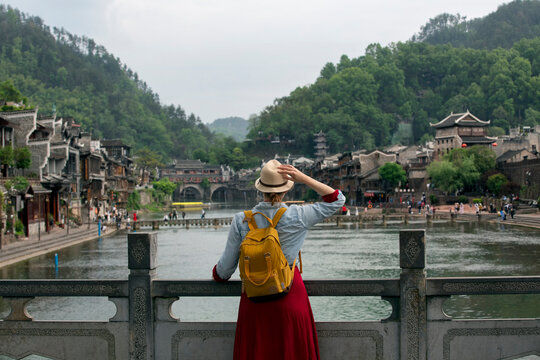 Young tourist dressed in red crossing the Tuojiang River in the historic Xiangxi Phoenix Ancient Town or Fenghuang Ancient Old Town, Hunan, China.