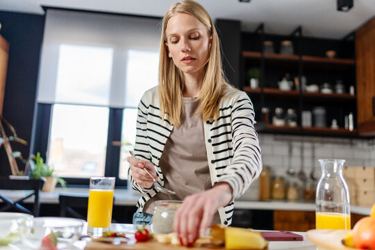 Young woman preparing a healthy breakfast with overnight oats, fresh fruit and cheese in a modern kitchen. Balanced nutrition, morning routine, healthy lifestyle and home cooking concept