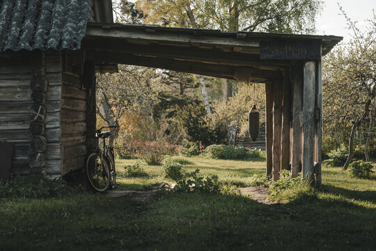 Laane County, Estonia - 19 May 2025: View of a rustic wooden log shed with a bicycle leaning against the wall and a hanging buoy in a lush garden on Vormsi island.