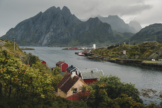 Sund, Norway - 04 September 2025: View of the coastal village of Sund nestled among dramatic mountains and rocky terrain with traditional red wooden houses along the fjord.