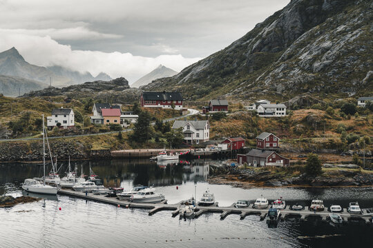 Sund, Nordland, Norway - 04 September 2025: View of the coastal village of Sund with colorful houses, a harbor filled with boats, and dramatic mountains under a cloudy sky.
