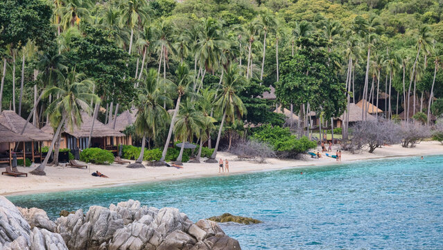 Ko Tao, Surat Thani, Thailand - 28 September 2025: View of Ko Tao beach with tropical palm trees, wooden bungalows, turquoise water, and rocky foreground.