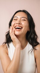 Naklejka premium Joyful young woman laughing with hand on face expressing happiness and carefree attitude in bright setting with her hand gently touching her face