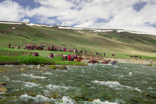 Skardu, Gilgit Baltistan, Pakistan - 24 July 2010: View of shepherds with horses crossing a river in Deosai National Park, with green meadows and snow-capped mountains.