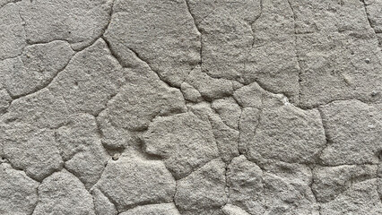 Close‑up of cracked roughcast plaster wall with irregular stucco patches and visible fissures, creating an abstract textured background with weathered architectural character. © Martins